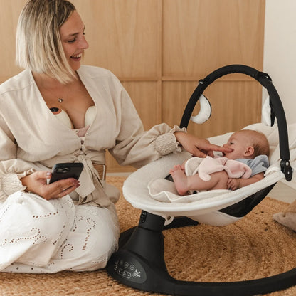 Een mama en haar baby in een stoel terwijl ze kolft met de Cura handsfree borstkolf